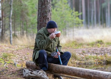 Nehrin kenarındaki balıkçı bir ağaç dalına oturur ve çay içer. Sonbahar zamanı, bulanık ağaç arka planında.
