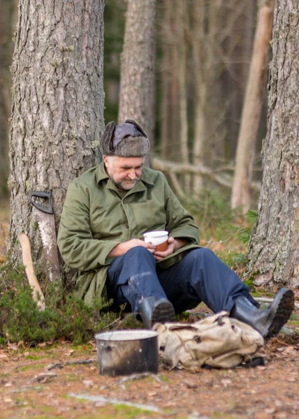 a forester in the forest drinks tea at rest, blurred forest background, bonfire with a pot over it, in the autumn forest