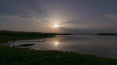 Gün batımından önce göl manzarası, bulutların arasından güneş ışınları, sakin su yüzeyi, göl çayırı önü, Burtnieki Gölü, Letonya