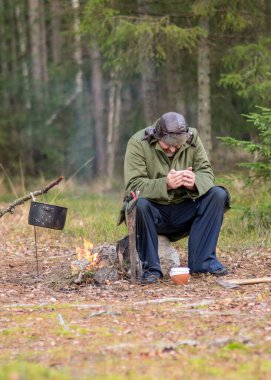 Ormandaki bir orman korucusu dinlenirken çay içer, ormandaki bulanık arka plan, üzerinde bir demlik olan şenlik ateşi, sonbahar ormanında.