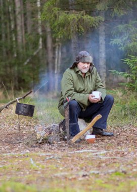 Ormandaki bir orman korucusu dinlenirken çay içer, ormandaki bulanık arka plan, üzerinde bir demlik olan şenlik ateşi, sonbahar ormanında.