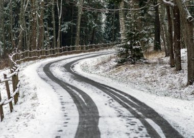 Karlı yollu kış manzarası, karla kaplı ahşap çitler, yol kenarındaki ağaçlar ve çalılar, kış günü