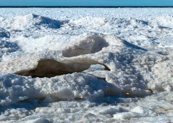 winter landscape by the sea, ice and stones in the dune area, in the distance the sea horizon, blue sky, winter