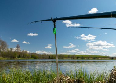 Bir göl ile bahar manzarası, göl kıyısında balıkçılık, sakin su yüzeyi ağaçlar ve gökyüzü yansımaları, göl kıyısındaki ilk yeşillik