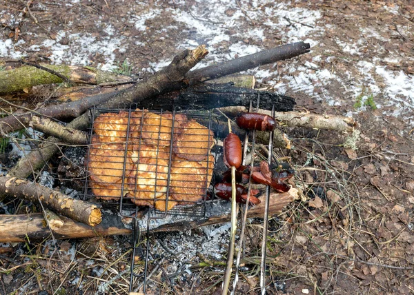 Karlı bir geçmişi ve piknik aksesuarları olan bir resim, kamp ateşi ve kışın kamp ateşinde pişirmek için gözleme ve sosisli demir şişler, kışın turist yemeği.