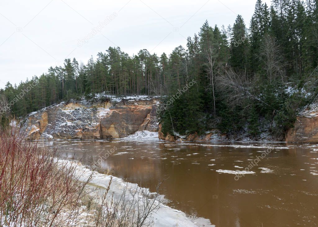 view of the river in early spring, sandstone outcrop, ice cubes in the water, river bank from the opposite bank, Erglu cliffs, river Gauja, Cesis, Latvia