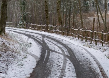 Karlı yollu kış manzarası, karla kaplı ahşap çitler, yol kenarındaki ağaçlar ve çalılar, kış günü