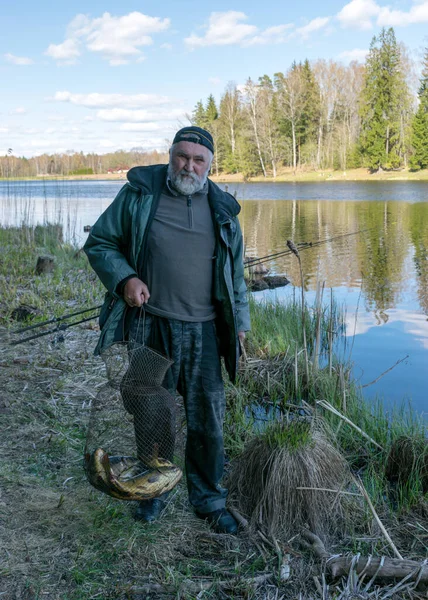 湖のある春の風景漁師は湖の岸で獲れた魚を見せ木と空の反射がある穏やかな水面湖の岸で最初の緑 — ストック写真