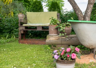 Yazın yeşil bahçe manzarası, paletlerden ev yapımı ahşap sandalye bahçede dinlenmek için, saksılarda renkli çiçekler açmak için.