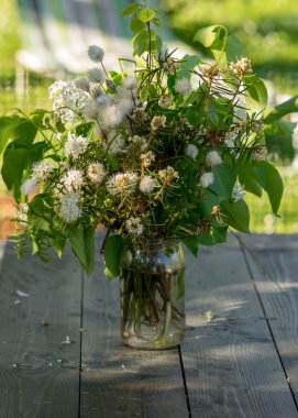 Tahta bir sehpada, cam bir kavanozda çiçek buketleri, doğada yaz.
