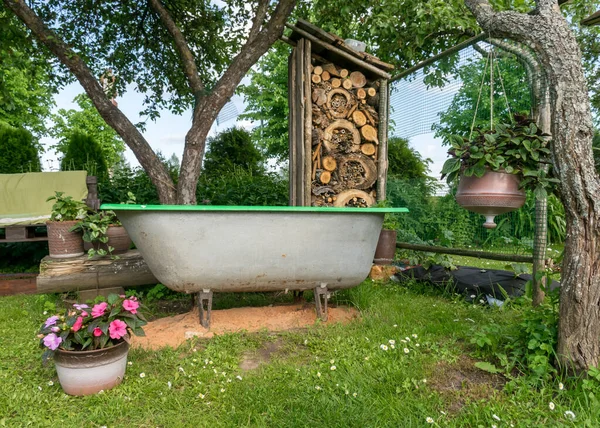 view of the garden in summer, wooden armchair from pallets, bath in the foreground in the foreground, a charming insect house, gardening concept
