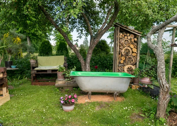 view of the garden in summer, wooden armchair from pallets, bath in the foreground in the foreground, a charming insect house, gardening concept