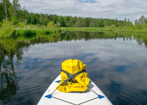 五彩缤纷的夏季风景从江边掠过 在前景上是一块水槽和一个黄色的橡胶袋 在水面上反射出云彩 在河岸上是绿树和青草 在拉脱维亚塞达斯河畔 — 图库照片