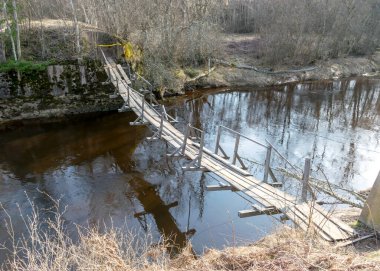Küçük, vahşi bir nehri olan bahar manzarası yaprakları olmayan çıplak ağaçlar, nehrin üzerindeki eski ahşap köprü, bahar günü.