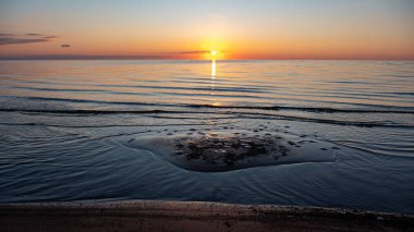 Deniz kenarında büyüleyici bir gün batımı, güneşin son ışınları sakin deniz yüzeyine yansıyor, parlak renkler, Vidzeme sahili, Letonya