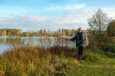 Nehir veya gölün kıyısında bir balıkçıyla manzara, balıkçılık konsepti, eğlence, doğada rahatlama, büyük hobi, sonbahar