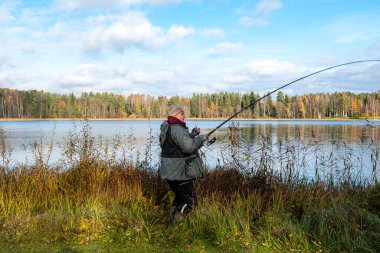 Nehir veya gölün kıyısında bir balıkçıyla manzara, balıkçılık konsepti, eğlence, doğada rahatlama, büyük hobi, sonbahar