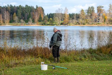 Nehir veya gölün kıyısında bir balıkçıyla manzara, balıkçılık konsepti, eğlence, doğada rahatlama, büyük hobi, sonbahar
