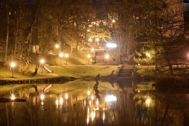 Karanlık sonbaharda şehir parkından renkli ve parlak sonbahar manzarası, suda büyüleyici yansımalarıyla aydınlanmış gölet, Cesis, Letonya, rudens
