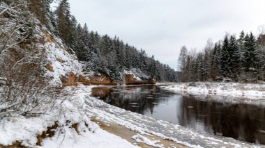 Nehir ve kumtaşı çıkıntılı kış manzarası, buzla donmuş nehir, ağaçlara düşen kar, Erglu kayalıkları, Cesis belediyesi, Letonya