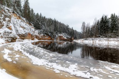 Nehir ve kumtaşı çıkıntılı kış manzarası, buzla donmuş nehir, ağaçlara düşen kar, Erglu kayalıkları, Cesis belediyesi, Letonya