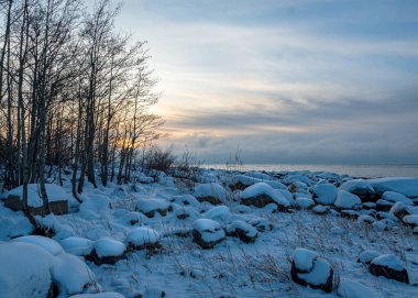 Deniz kenarındaki renkli kış manzarası, deniz kıyısındaki donmuş taşlar, günbatımı renkleri, kar ve buz, Letonya, Vidzeme 'deki Rocky sahili.