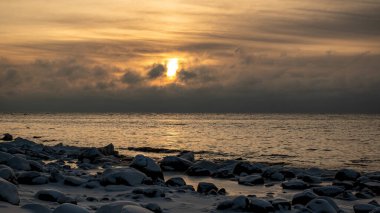 Deniz kenarındaki renkli kış manzarası, deniz kıyısındaki donmuş taşlar, günbatımı renkleri, kar ve buz, Letonya, Vidzeme 'deki Rocky sahili.