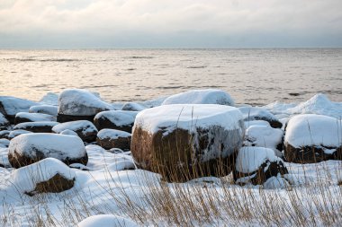 Deniz kenarındaki renkli kış manzarası, deniz kıyısındaki donmuş taşlar, günbatımı renkleri, kar ve buz, Letonya, Vidzeme 'deki Rocky sahili.