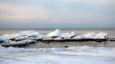 Deniz kenarındaki renkli kış manzarası, deniz kıyısında buz saçakları olan donmuş taşlar, günbatımı renkleri, kar ve buz, Letonya, Vidzeme 'deki Rocky sahili.