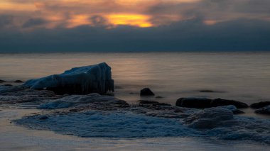 Deniz kenarındaki renkli kış manzarası, deniz kıyısındaki donmuş taşlar, günbatımı renkleri, kar ve buz, Letonya, Vidzeme 'deki Rocky sahili.