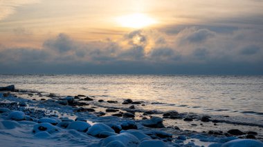 Deniz kenarındaki renkli kış manzarası, deniz kıyısındaki donmuş taşlar, günbatımı renkleri, kar ve buz, Letonya, Vidzeme 'deki Rocky sahili.