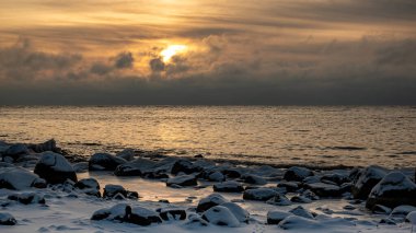 Deniz kenarındaki renkli kış manzarası, deniz kıyısındaki donmuş taşlar, günbatımı renkleri, kar ve buz, Letonya, Vidzeme 'deki Rocky sahili.