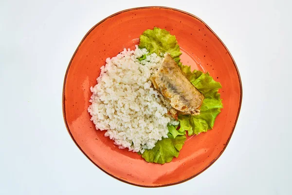Beyaz arka planda yuvarlak turuncu bir tabakta bir parça balık ve marul yapraklı haşlanmış pirinç lapası..
