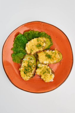 Deri ve peynirli üç dilim kabak pişirdim. Beyaz bir zemin üzerinde yuvarlak turuncu bir tabakta marul yaprağı ile ince doğranmış dereotu serpiştirdim..