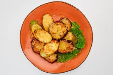 Beyaz arka planda yuvarlak turuncu bir tabakta peynirli, sarımsaklı ve marullu 11 dilim kabak ve patlıcan..