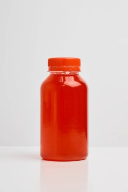 Transparent plastic bottle with an orange lid, with lingonberry juice inside on a white background.