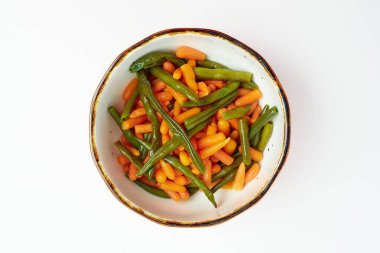 Haşlanmış yeşil fasulye garnitürü, beyaz arka planda yuvarlak beyaz bir tabakta taze havuçlar..