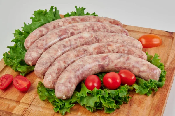 Meat kupatas five pieces with red cherry tomatoes and green lettuce leaves on a rectangular wooden cutting board on a white background.