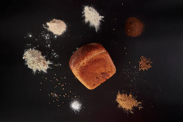 One loaf of bread on a black background with eight piles around spices and flour.