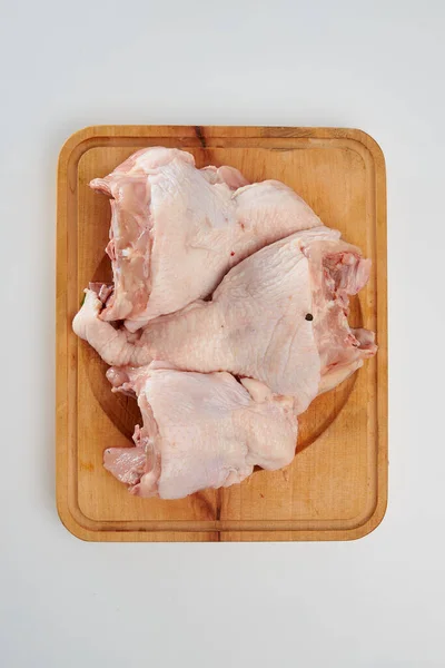 Three fresh chicken backs with black pepper peas on a rectangular wooden chopping board on a white background.