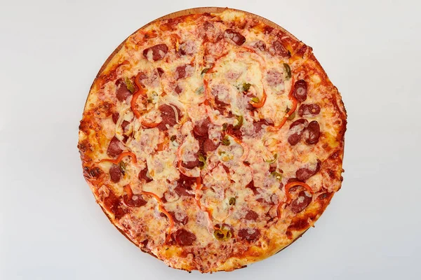 A whole round pizza with salami sausage, onions, red peppers, cucumbers and cheese on a white background.