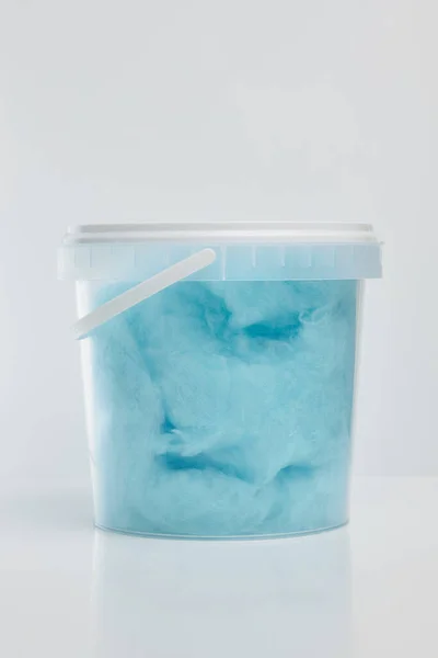 Blue sweet cotton candy in a transparent plastic bucket with a lid and a white handle on a white background.