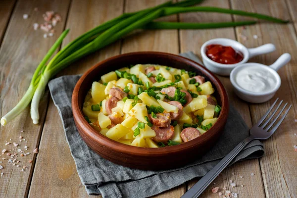 A hearty lunch: Baked potatoes with sausages in a clay plate on a wooden table