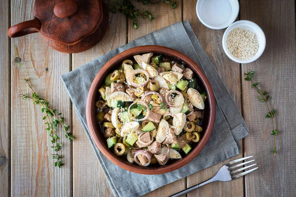 Zeytinli lezzetli salata ve ahşap arka planda kil kasede morina ciğeri.