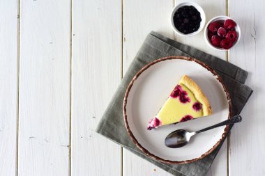 Beyaz bir masada lezzetli ahududu ve yaban mersinli turta. Tahta bir masada beyaz bir tabakta bir parça çilekli turta.