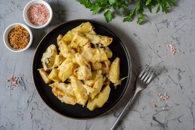 Sıcak bir atıştırmalık: baharat ve peynirle pişirilmiş patates dilimleri. Gri arka planda güzel bir tabakta patates ve peynir. Üst görünüm