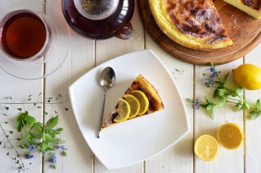 Beyaz tabakta bir parça peynirli turta, bir fincan çay, beyaz masada bir parça peynirli turta.