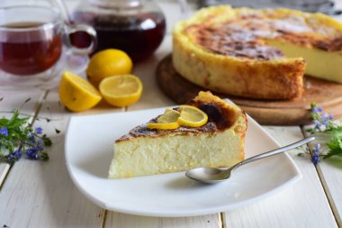 Tatlı atıştırmalık: güzel bir tabakta limonlu bir dilim peynirli turta, bir peynirli turta ve beyaz bir masada bir fincan çay.