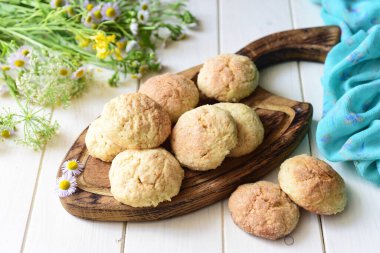 Tatlı atıştırmalık: Tahtadaki şekerli kurabiyeler ve beyaz masadaki çiçekler..