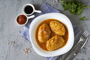 Gri arkaplanda beyaz bir tabakta domates soslu et pirzolası. Güzel bir tabakta domuz köftesi. Üst görünüm